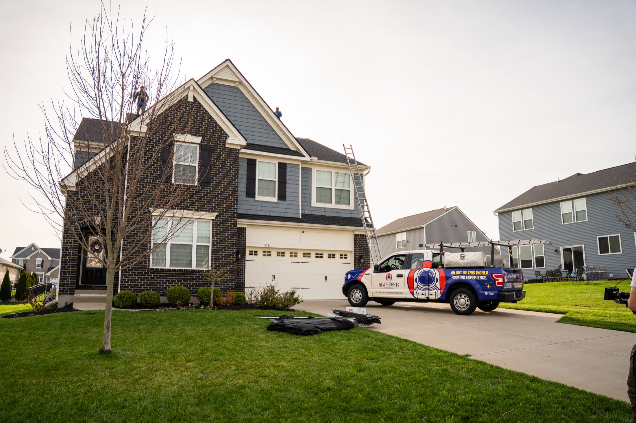 New Heights Roofing crew on a roof with the branded truck in the driveway